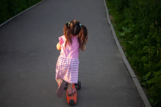 Child on scooter. Girl rides down road. Details of walk with child. Scooter for baby.