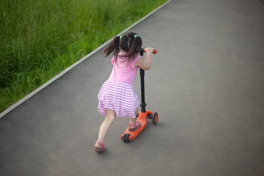 Child on scooter. Girl rides down road. Details of walk with child. Scooter for baby.