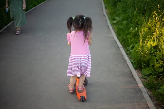 Child on scooter. Girl rides down road. Details of walk with child. Scooter for baby.