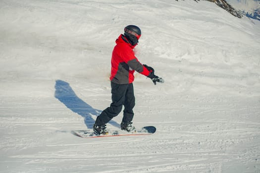 A snowboarder rides on a slope. Rest on the top of the mountain. Mountain ski resort. The guy is rolling down the mountain. Hobbies for young people.