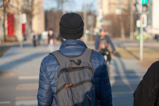 A guy with a backpack from the back. A man with a hat and a backpack. An unknown person walks through the city.