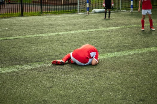 Footballer fell. Child plays football. Injury on field. Game details. Foot injury in sports.