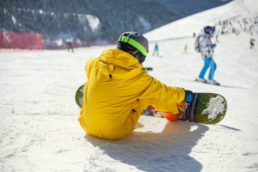 A snowboarder rides on a slope. Rest on the top of the mountain. Mountain ski resort. The guy is rolling down the mountain. Hobbies for young people. Holidays in the winter on a slope for snowboarding.