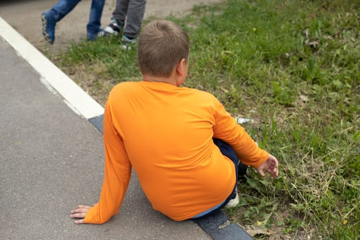 Child is sitting on asphalt. Boy on road. Schoolboy is tired. Rest in summer.