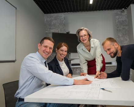 Designers engineers at a meeting discuss working drawings. Four smiling business people are looking at the camera