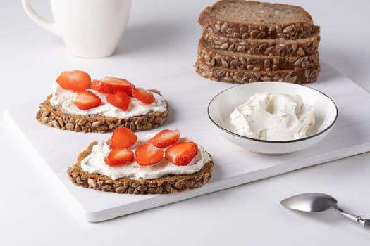 Rye bread with cream cheese and strawberry on a white table. Whole grain rye bread with seeds.