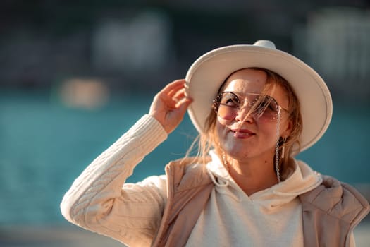 Happy blonde woman in a white suit and hat posing at the camera against the backdrop of the sea.