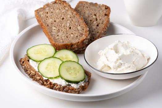 Rye bread with cream cheese and cucumbers on a white table. Whole grain rye bread with seeds.