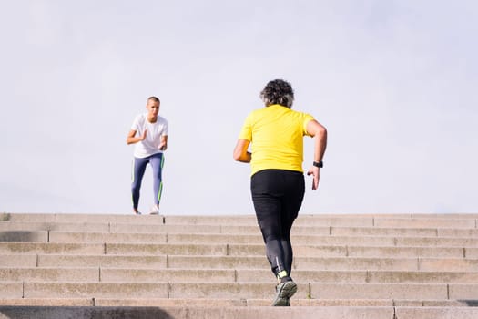 rear view of an unrecognizable sports old man training on stairs while receiving encouragement from his personal trainer, concept of active and healthy lifestyle in middle age