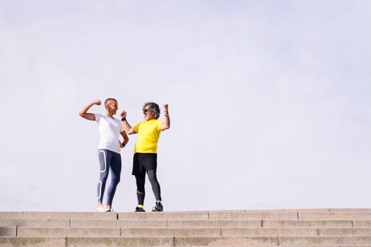 senior man and his personal trainer celebrate the success of the effort by showing muscle and smiling happy, concept of active and healthy lifestyle in middle age, copy space for text