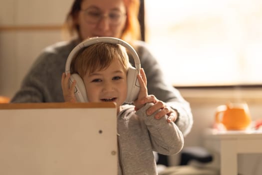 A young boy wearing headphones while sitting on kitchen with mother