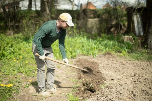 Guy digs soil with shovel. Digging up ground for planting. Work in garden. Life in countryside. Man works.