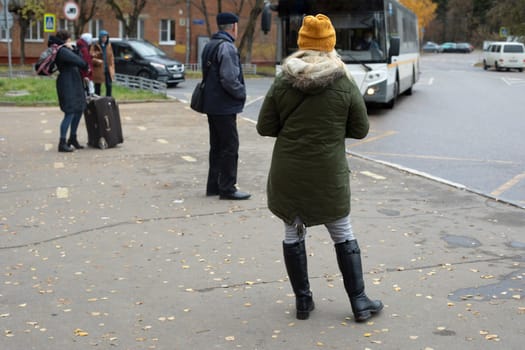 People are waiting for bus in fall. People at bus station. Public transport in city. People at bus stop. Details of city life.