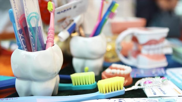 A large model of human jaw with white teeth, colorful toothbrushes, and a toy lying on the table, children dental clinics concept. Close up for the dental instruments.