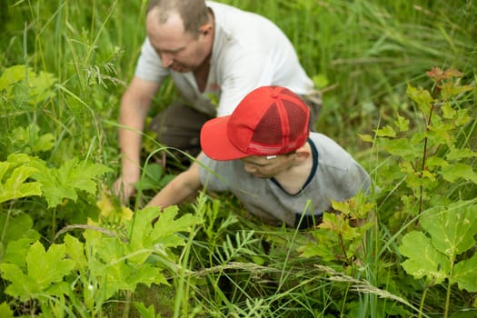 Father and son pick berries. Peasants pick fruit. Poor people are looking for food. Baby with dad in green grass.