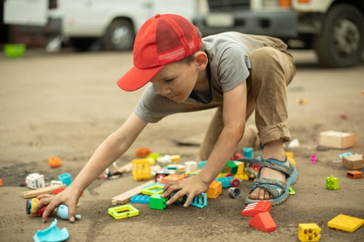 Child collects toys in box. My son scattered things. Boy plays alone in street. Poor child takes toy.