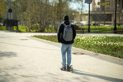 Guy rides scooter, guy rides around town on scooter. Man with backpack on street.