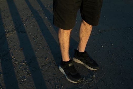 Legs of guy in black shorts and black sneakers. Persons feet stand on ass. Shorts in fashion. Summer clothes.