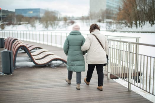 Girls walk in park in winter. Girlfriends on street. People in city. Two girls walk along promenade.