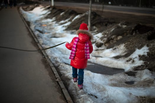 Child walks in red jacket. Girl in winter jacket. Child in city in winter.