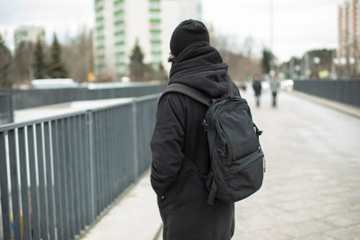 Guy in black clothes on street. Man's black backpack. European in city. Style of dress is all black.