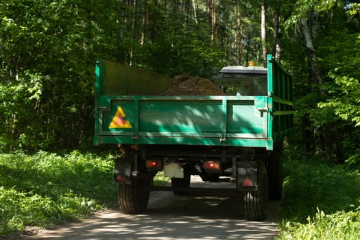 Tractor trailer. Cart by truck. Car drives through park. Rural machinery.