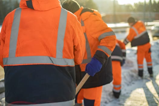 Workers remove snow with shovels. Workers in orange suits. City cleaning service. Snow removal details.