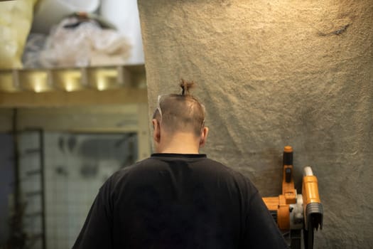 Guy with ponytail on his head. Short hair. Man in workshop.
