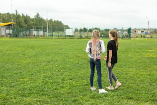 Children on lawn. Girls talk outside in summer. Teenagers walk on green grass. Mowed lawn under your feet.