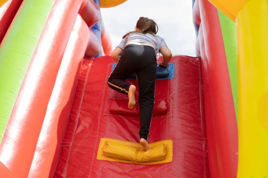 Child on slide. Inflatable slide for children. Baby climbs up. Play area in summer. Inflatable structure in park.