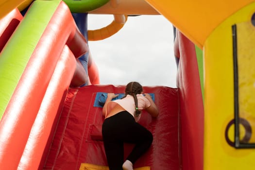 Child on slide. Inflatable slide for children. Baby climbs up. Play area in summer. Inflatable structure in park.