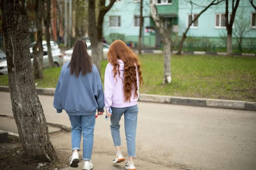 Two girls in jeans. Walk around city. People on street. Girls are walking. Long hair.