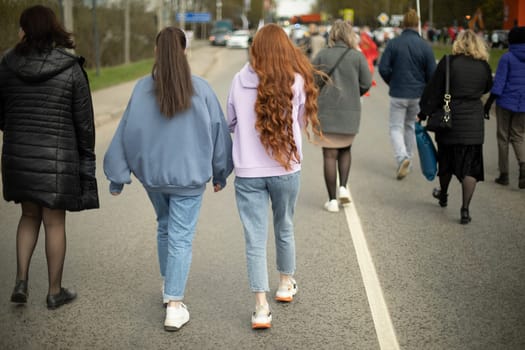 Two girls in jeans. Walk around city. People on street. Girls are walking. Long hair.