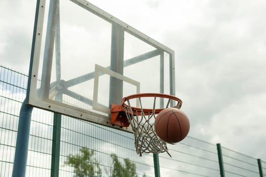 Throwing ball into hoop. Basketball flies into net. Basketball details. Sports ground on cloudy day.