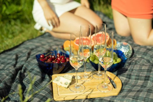 Picnic in summer in park. Food on background of girls. Champagne glasses. Details of rest in park. Food on street. Fruits mime drinks.