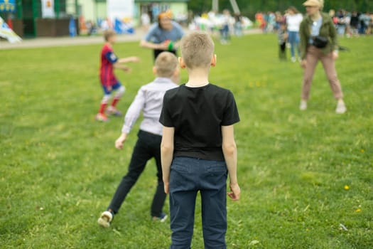 Child on green grass. Schoolboy plays on lawn in summer. Active holidays. Child from behind.