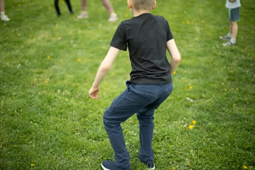 Child on green grass. Schoolboy plays on lawn in summer. Active holidays. Child from behind.