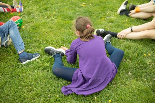 Teenage girl sits on green lawn. Girl in park. Rest on summer day