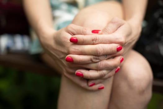 Red nail polish. Girl's hands are on her lap. Lacquer is red. Details of manicure.