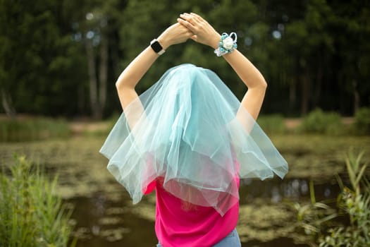 Girl in park. Girl in summer on shore of pond. Blue cape on head. Transparent veil on hair. Jeans and t-shirt.