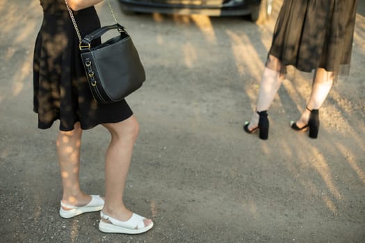 Girl with black bag in black dress on street. Girls in parking lot. Clothing details. Young girls in summer in city.