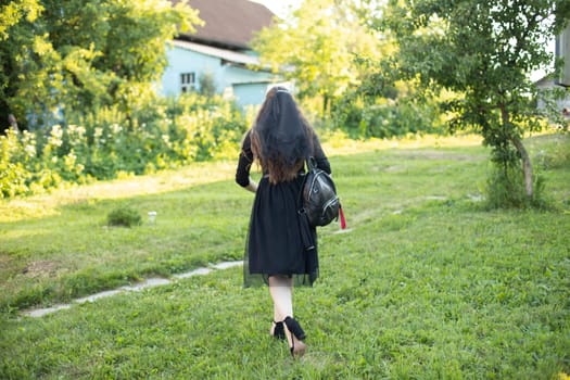 Girl in black dress stands alone on grass. Girl at party. Mourning dress. Black clothes.