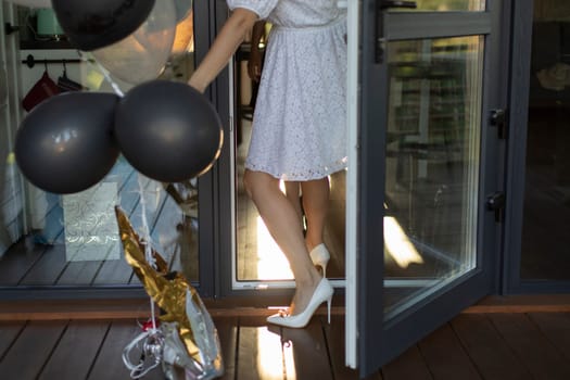 Girl in balloons enters house. Bride is preparing for wedding. White dress on girl. White shoes. Black balls.