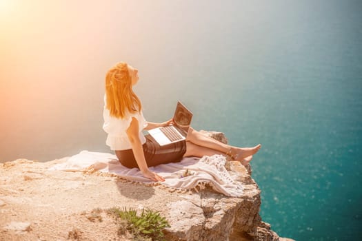 Freelance woman working on a laptop by the sea, typing away on the keyboard while enjoying the beautiful view, highlighting the idea of remote work