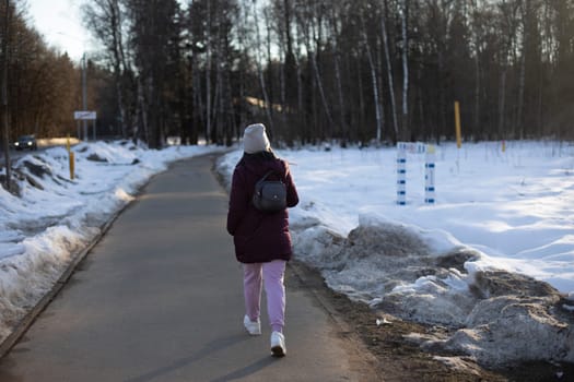 Girl in winter in park. Woman walks down road. Walk in afternoon.