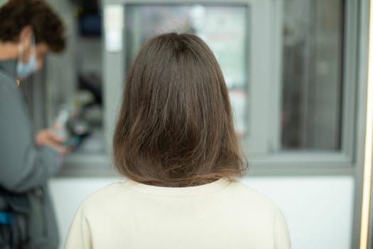 Girls hair from back. Girl in line. Brunette on street. White sweater. Uncolored hair on head.