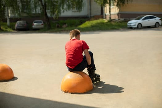 Child wears roller skates. Mask in red T-shirt. Schoolboy alone. Preparation for arrival. Roller skates in summer.