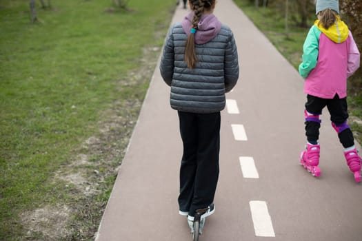 Child on scooter rolls in park. Child on scooter. Walk with children in city. Bike path made of asphalt.