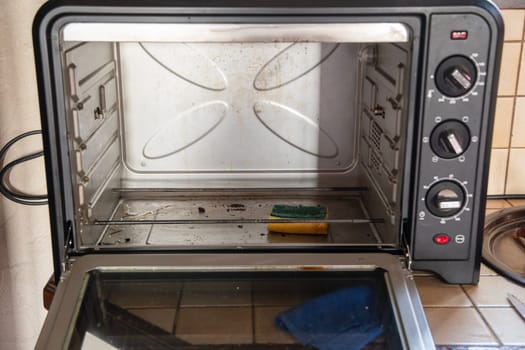 Open Dirty oven with burnt spots of food debris on the glass, on the tray and on the walls, freestanding oven on the table in the kitchen, High quality photo