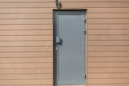 Technical entrance to building. Grey door. Narrow door in wall.